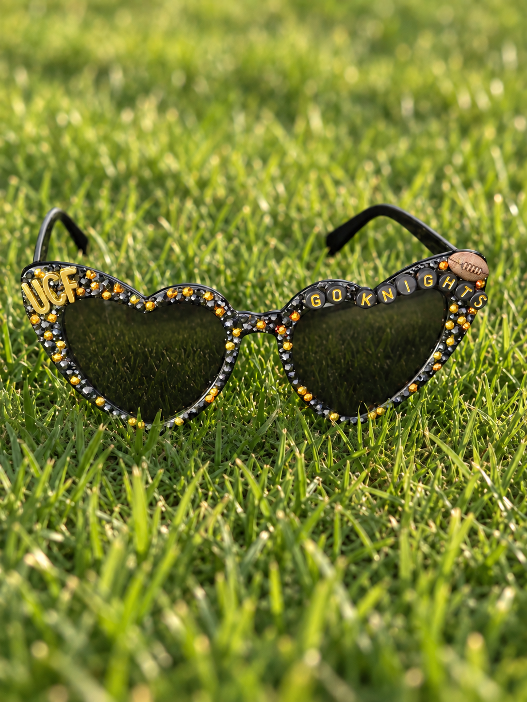 Black heart-shaped rhinestone sunglasses with black and gold beading and a football charm